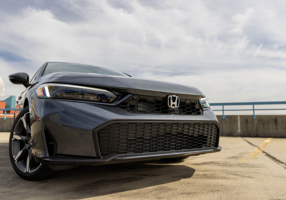 2025-honda-civic-hybrid.png Honda Civic Hybrid parked on top of a parking deck with a cloudy sky in the background