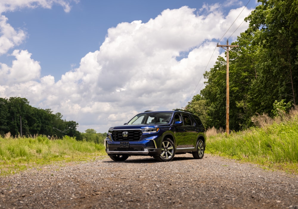 Blue 2025 Honda Pilot parked on a gravel road with trees and powerlines in the background