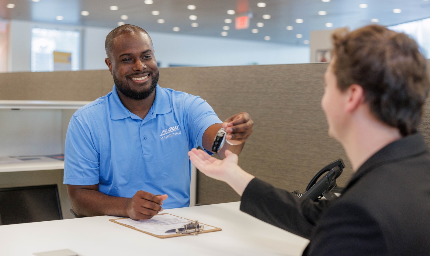 Flow Auto employee passing car keys to a customer over a desk