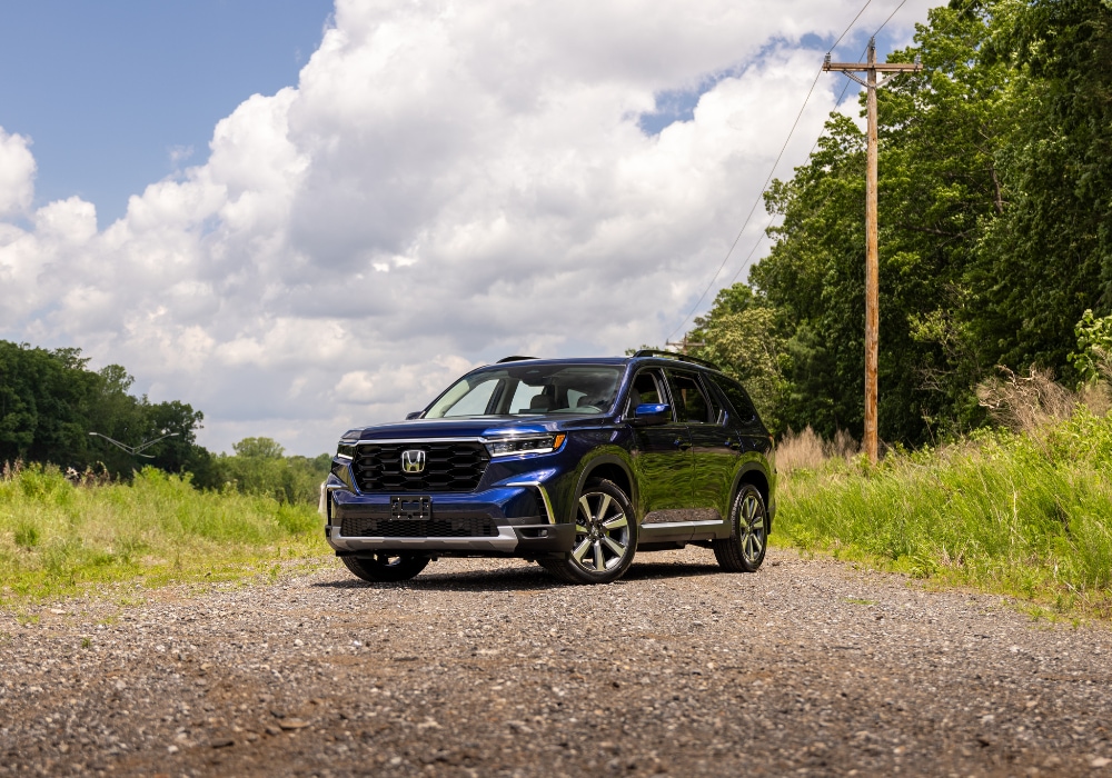 honda-pilot-specs.png 2025 Honda Pilot parked on a gravel road with trees and clouds in the background