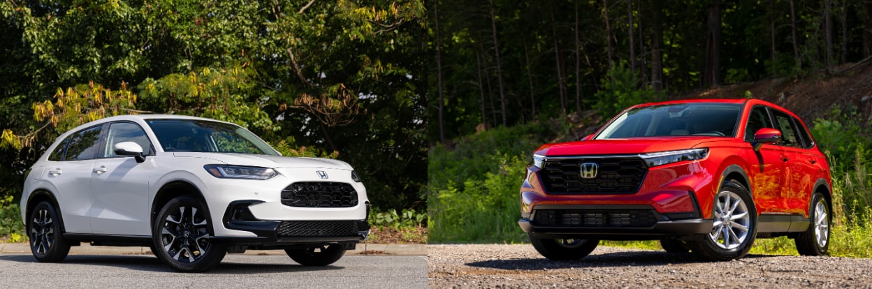 White Honda HR-V next to a red Honda CR-V. Both cars are parked on a paved surface with trees in the background