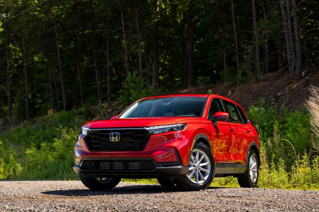 Red 2025 Honda CR-V parked on a gravel road with a wooded area in the background