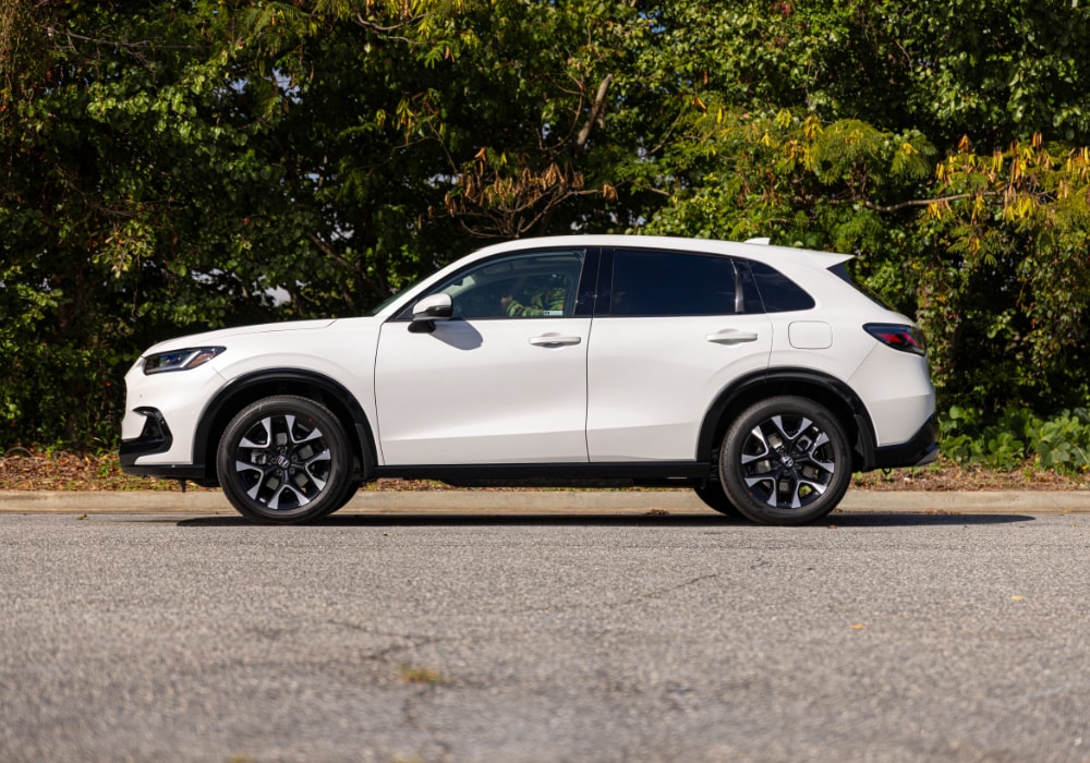honda-hr-v-fuel-economy.png Driver's side view of a 2025 Honda HR-V parked on a paved road in front of a wooded area