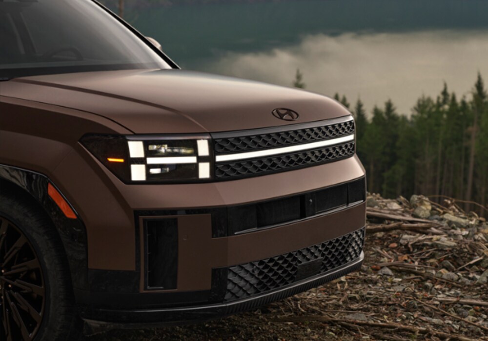 Close up photo of the 2025 Hyundai Santa Fe. The SUV is brown and there are trees in the background