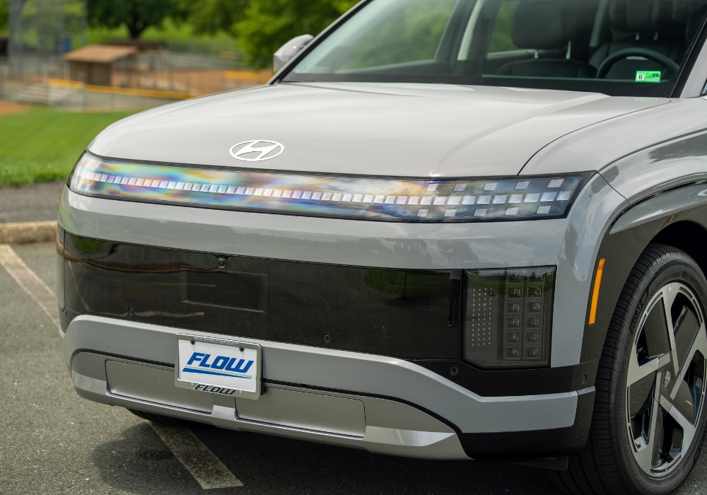 Front grille of a 2026 Hyundai IONIQ 9. The SUV is gray and there is a Flow license plate attached to the front of the car