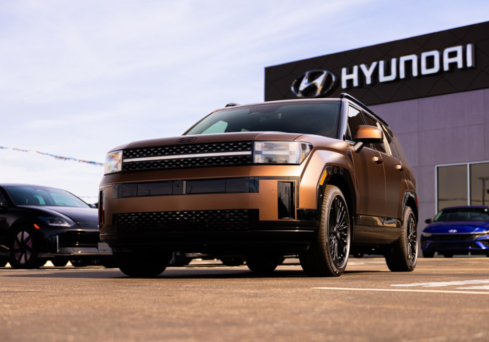 2026 Hyundai Santa Fe Hybrid parked in front of the Flow Hyundai of Statesville dealership. The SUV is orange