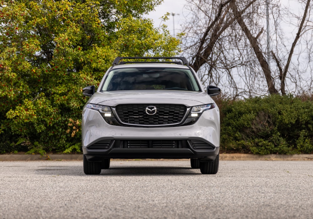 Front view of the 2026 Mazda CX-5 SUV parked in an empty lot with trees in the background
