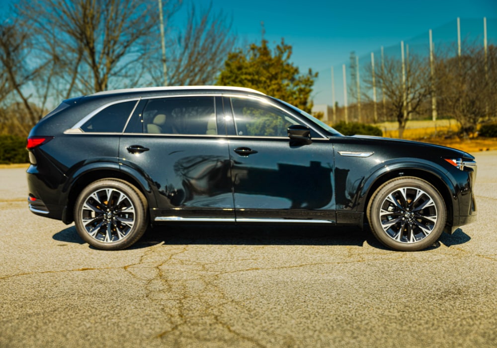 Passenger side view of a dark colored Mazda CX-90 SUV parked on a paved surface