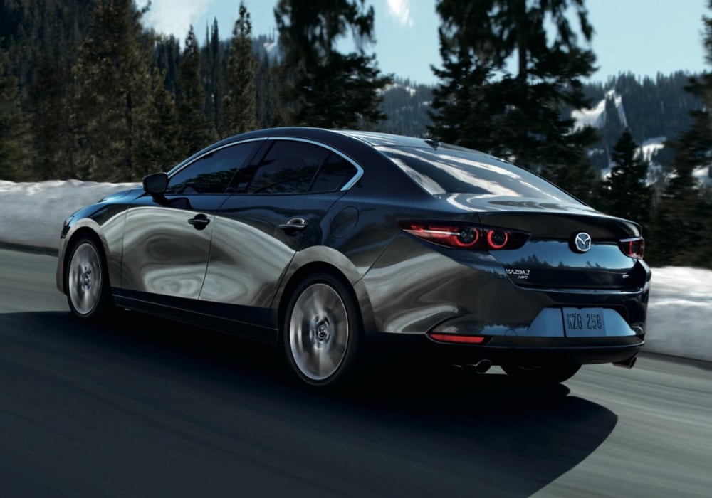Rear view of a black 2026 Mazda3 sedan driving down a road