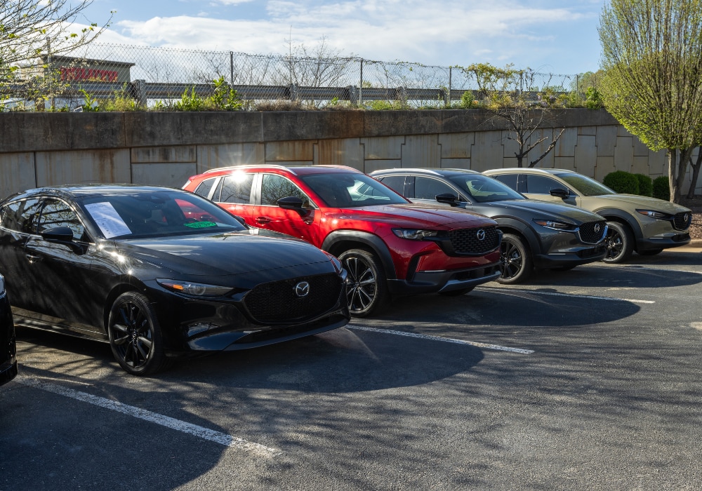 mazda-demo-vehicles-greensboro-nc.png A lineup of Mazda cars for sale parked in the lot of the Flow Mazda of Greensboro dealership