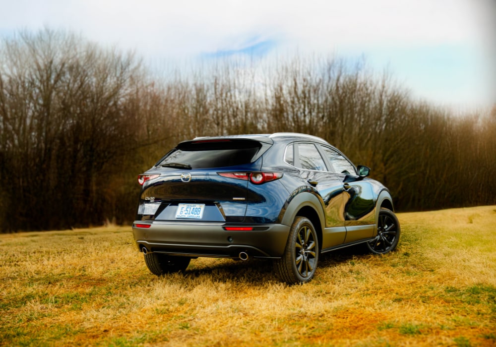 Rear exterior photo of the new Mazda CX-90 SUV parked in a grassy area with trees in the background