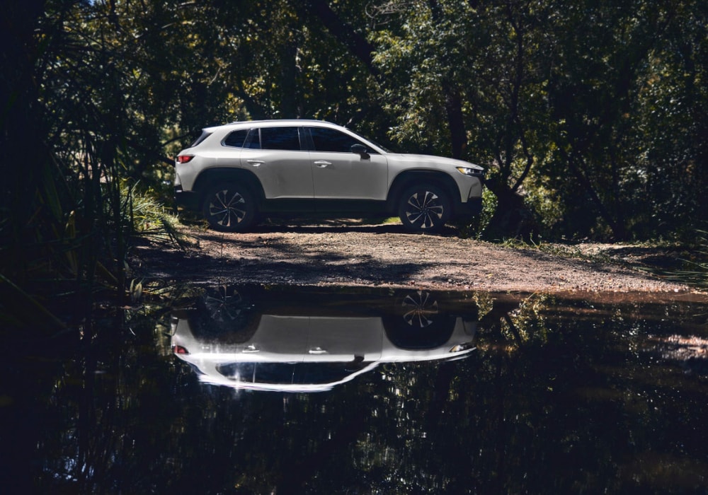 Passenger side view of a 2026 Mazda CX-50 Hybrid parked in a wooded area