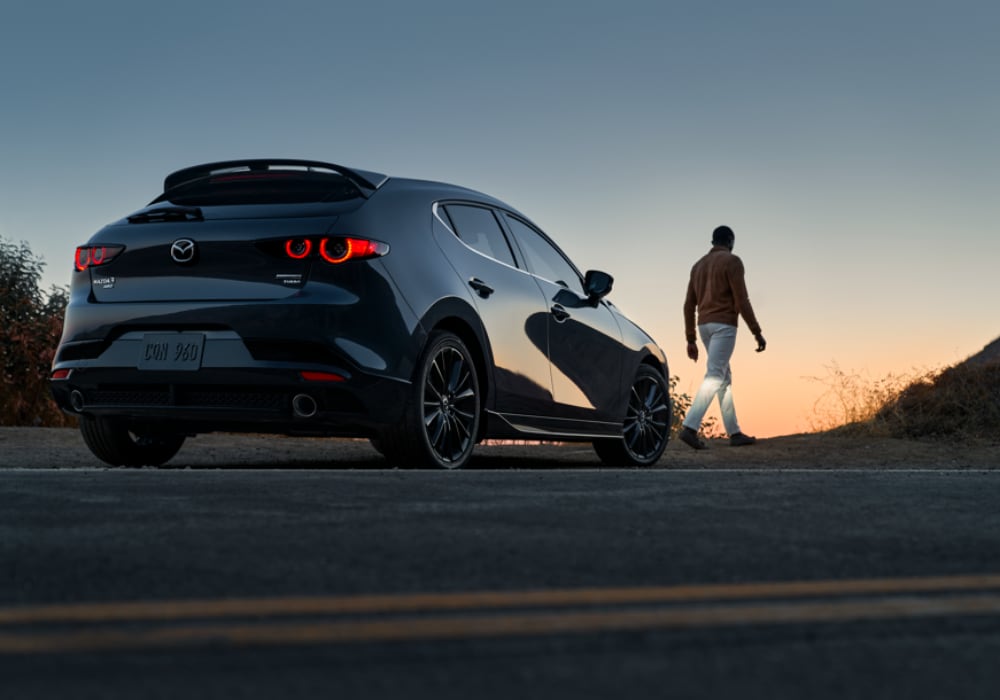 new-mazda3-hatchback-for-sale.png Mazda3 Hatchback parked on the side of the road facing away from the camera. There is a person walking away from the car