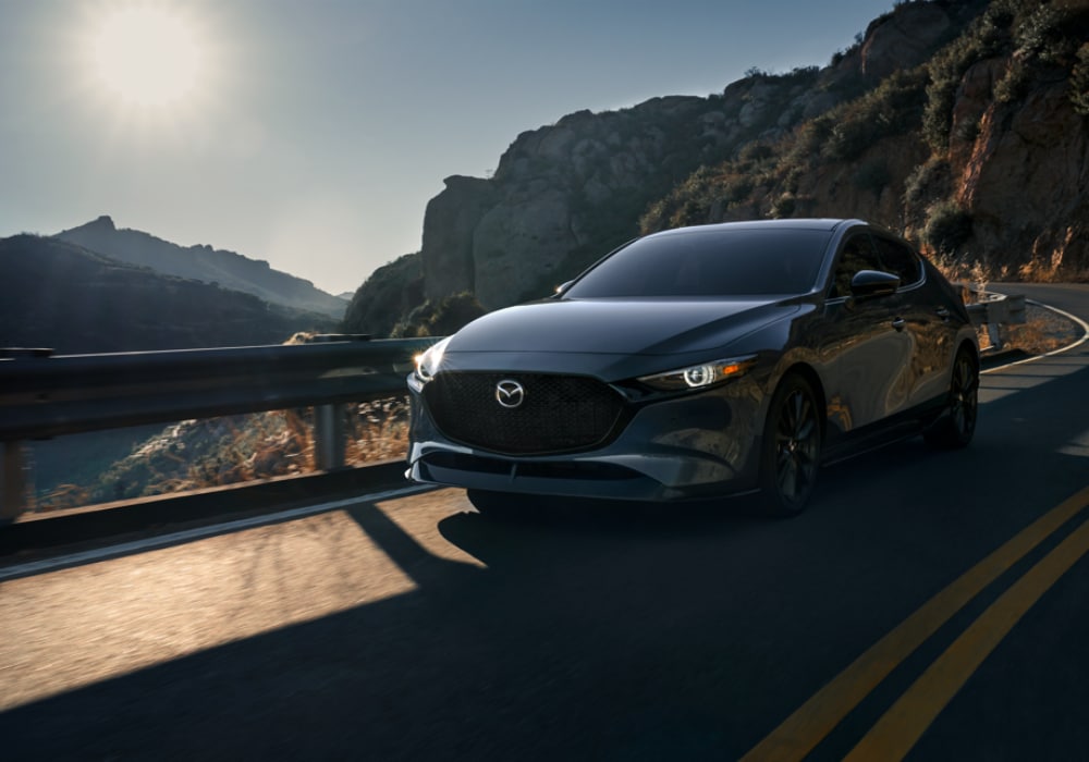 mazda3-for-sale-greensboro.png Black Mazda# driving down a road toward the camera. There are mountains in the background