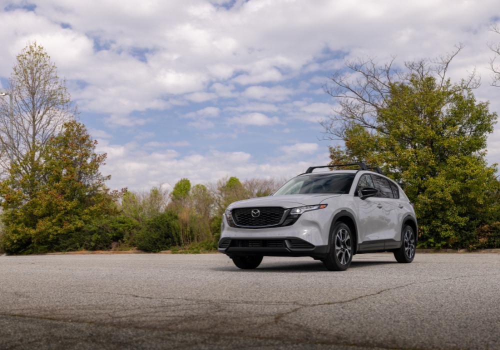The 2026 Mazda Cx-5 parked in an empty lot in front of trees. The SUV is gray