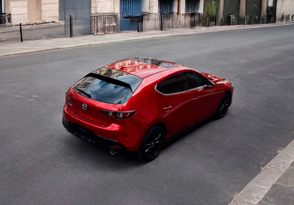 Red Mazda3 Hatchback driving down a paved road
