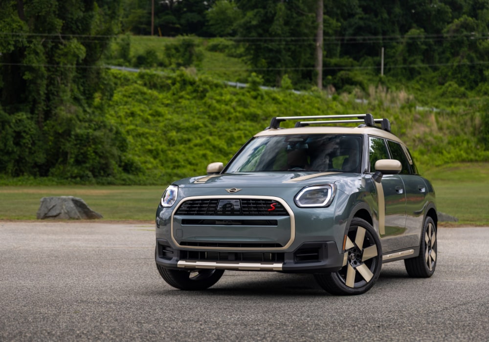 2026 Mini Cooper Countryman parked in front of a lush background. The car is gray with gold accents