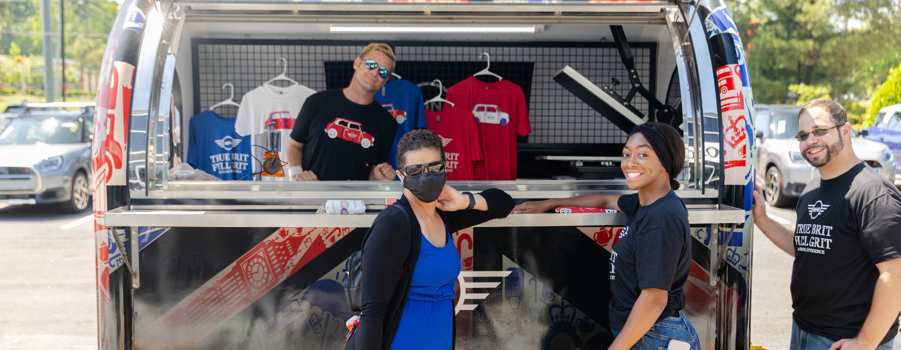 Four people looking at the camera and smiling in front of Mini True Brit Full Grit merch
