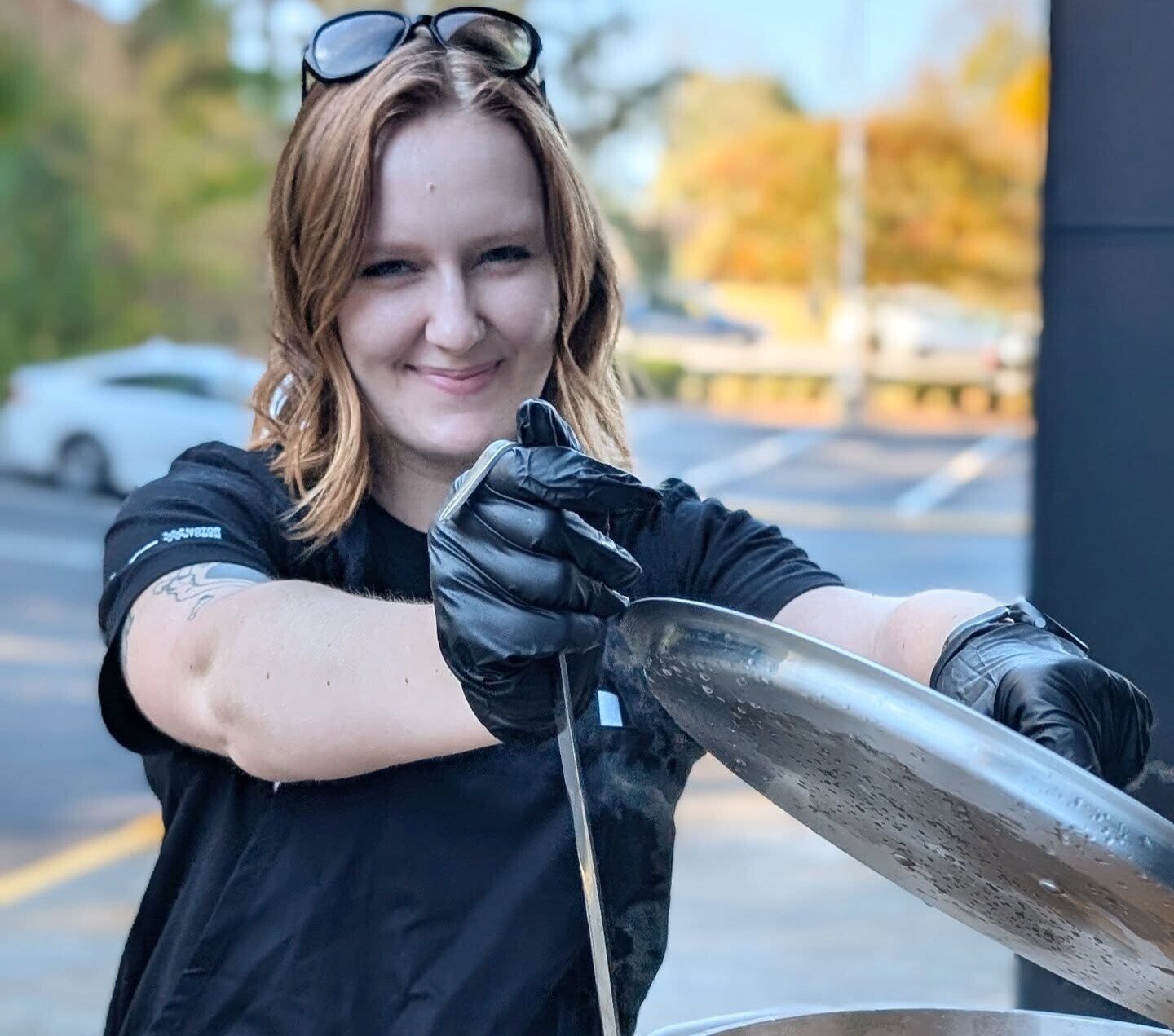 A woman smiling at the camera and holding a ladle next to a large pot