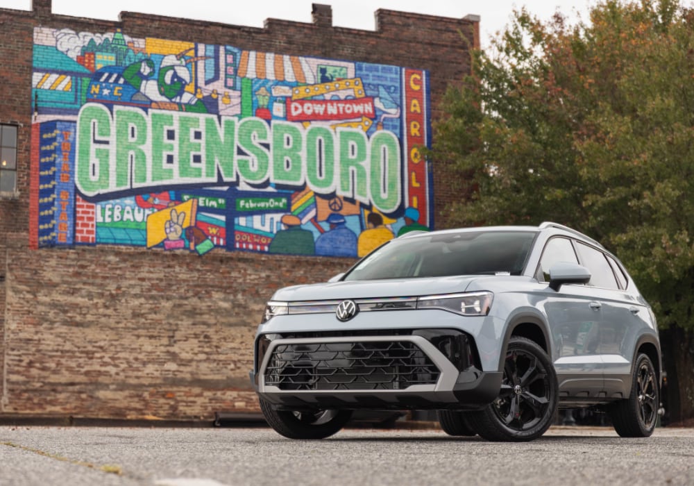 Silver Volkswagen Taos parked in front of a brick wall with colorful graffiti and the word Greensboro
