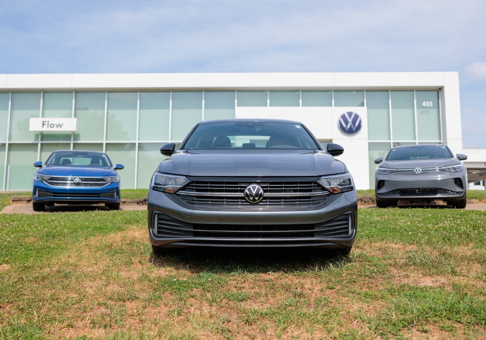 Three Volkswagen SUVs parked on a grassy hill in front of the Flow Volkswagen of Winston-Salem dealership