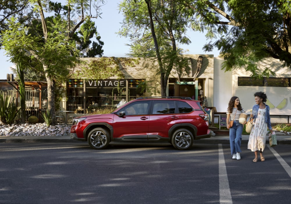 2026 Subaru Forester parked on a street with a store in the background. There are two women in a crosswalk