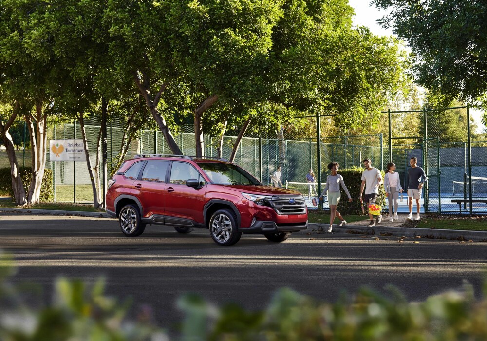 A red 2026 Subaru Forester parked outside a tennis court. A group of people are walking towards the SUV