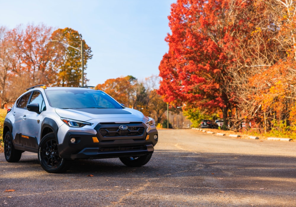 Silver Subaru SUV for sale parked on an empty road with trees in the background
