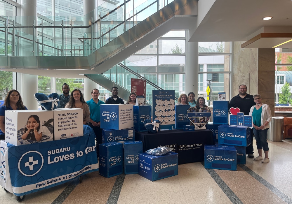 A group of people standing inside the lobby of a hospital. There are donation boxes from Flow Subaru of Charlottesville in front of them