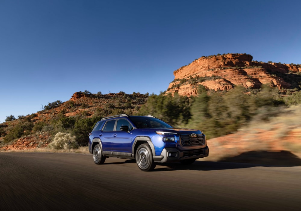 Blue 2026 Subaru Outback driving with mountains in the background
