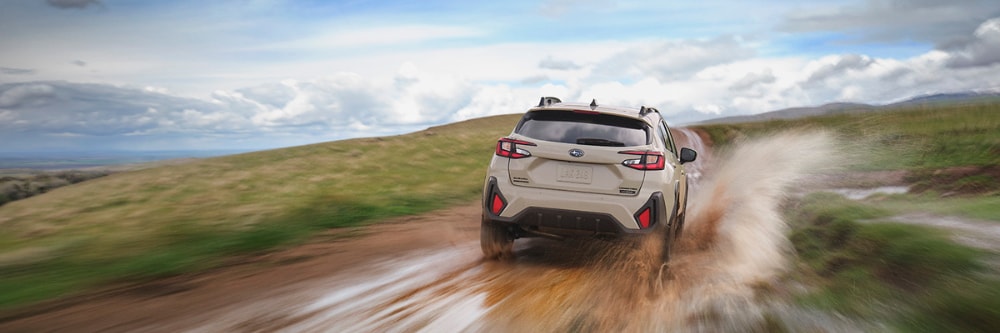 2026 Subaru Crosstrek Hybrid driving away from the camera and down a dirt road