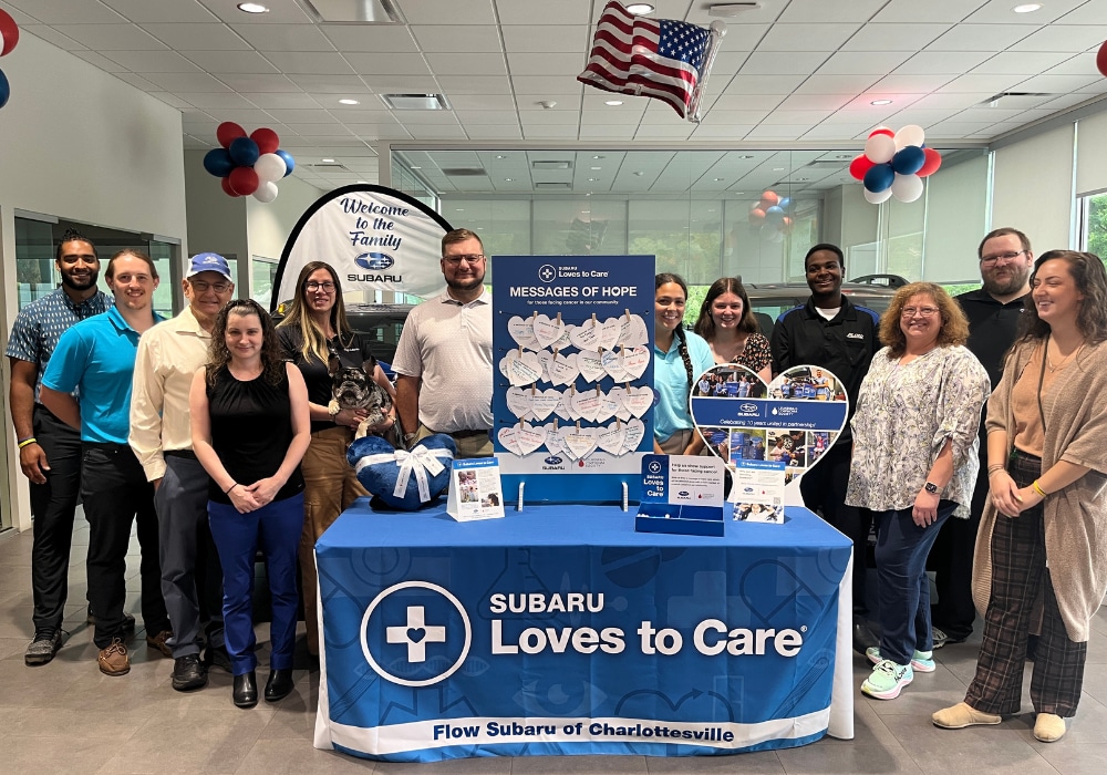 Dealership employees standing behind a table that says Subaru Loves to Care