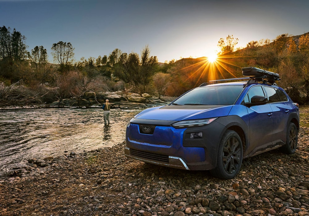 Subaru Trailseeker SUV EV parked next to a stream of water. There is a person standing in the water and fishing.