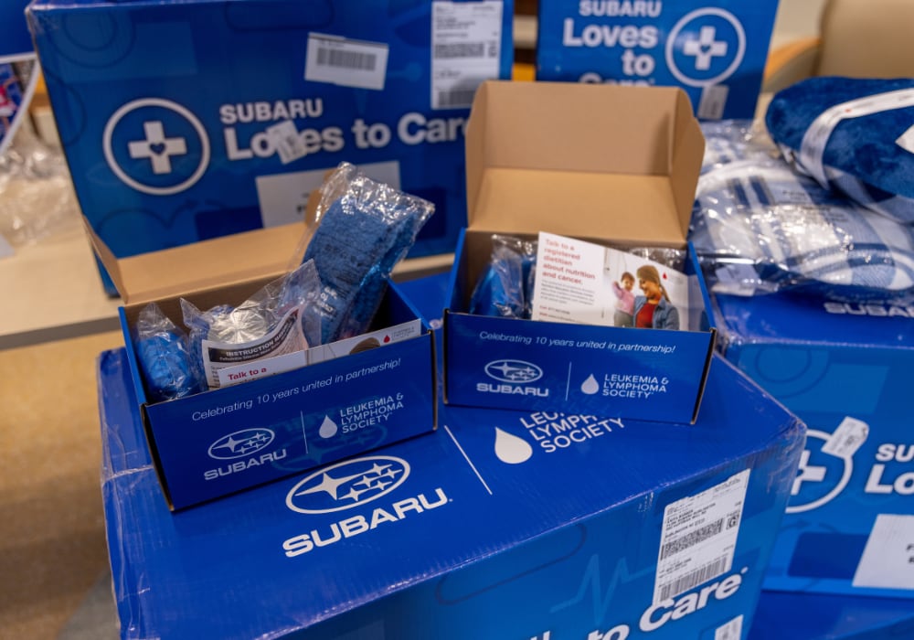 Subaru care packages stacked on top of each other, along with blankets. The Subaru Loves to Care logo is visible on each box
