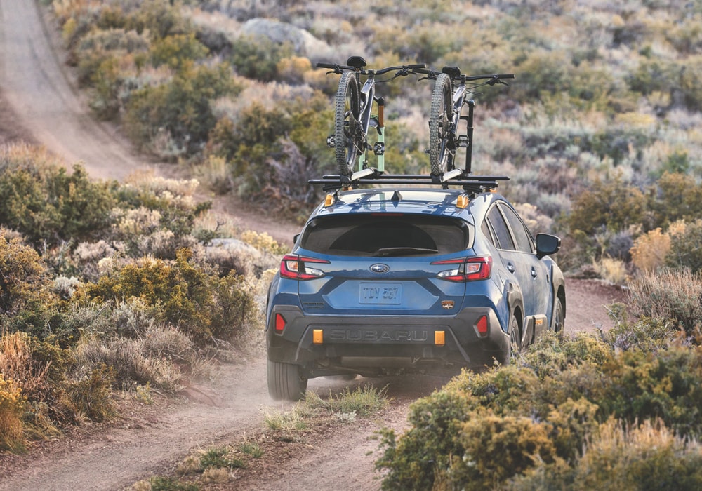 New Subaru Crosstrek Wilderness driving away from the camera down a dirt path. There are two bikes attached to the roof rack of the SUV