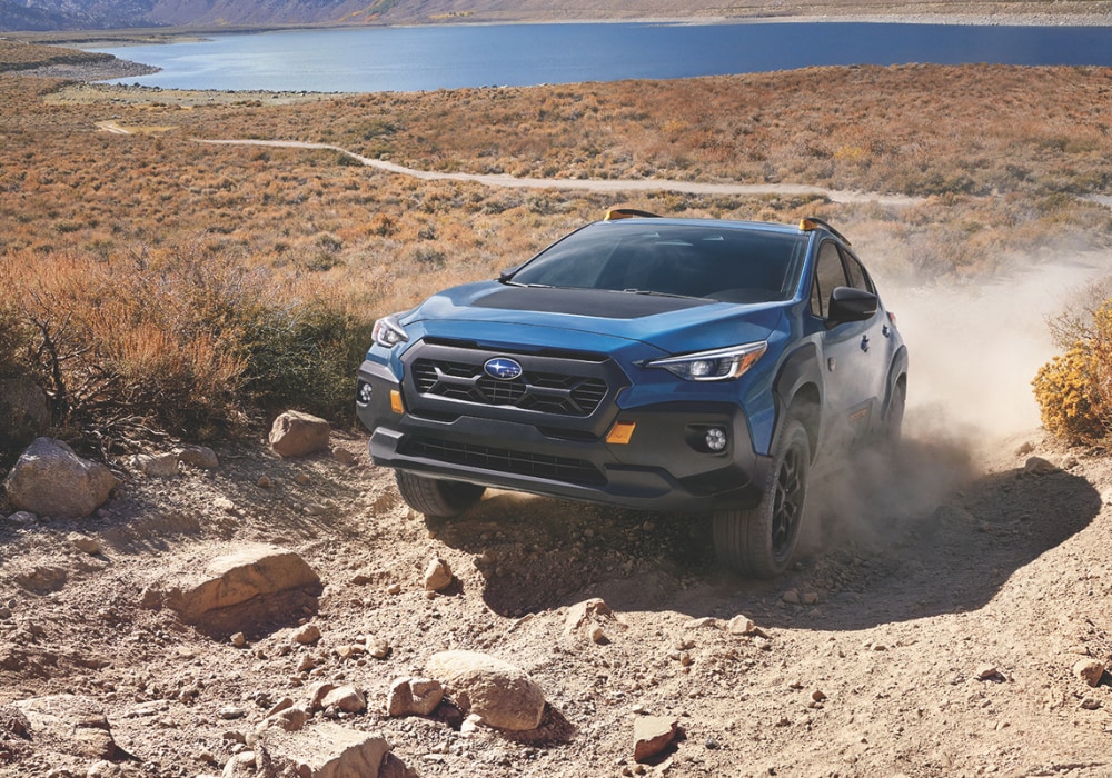 Blue Subaru Crosstrek Wilderness driving up a dirt path with a large body of water in the background