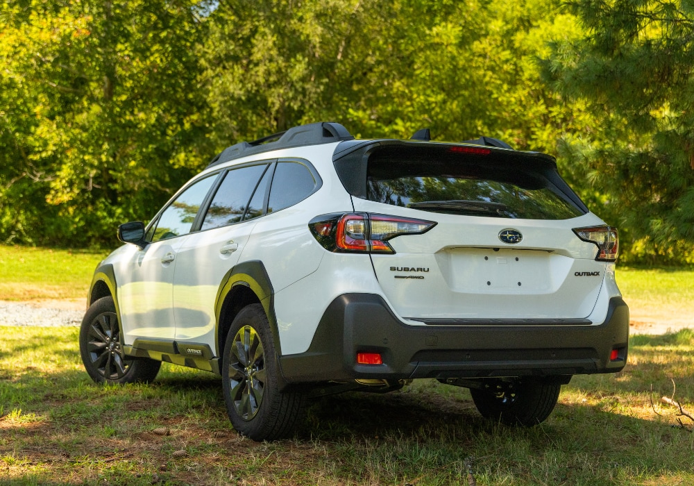 Rear exterior view of a new Subaru Outback for sale. The SUV is white and parked in a grassy area