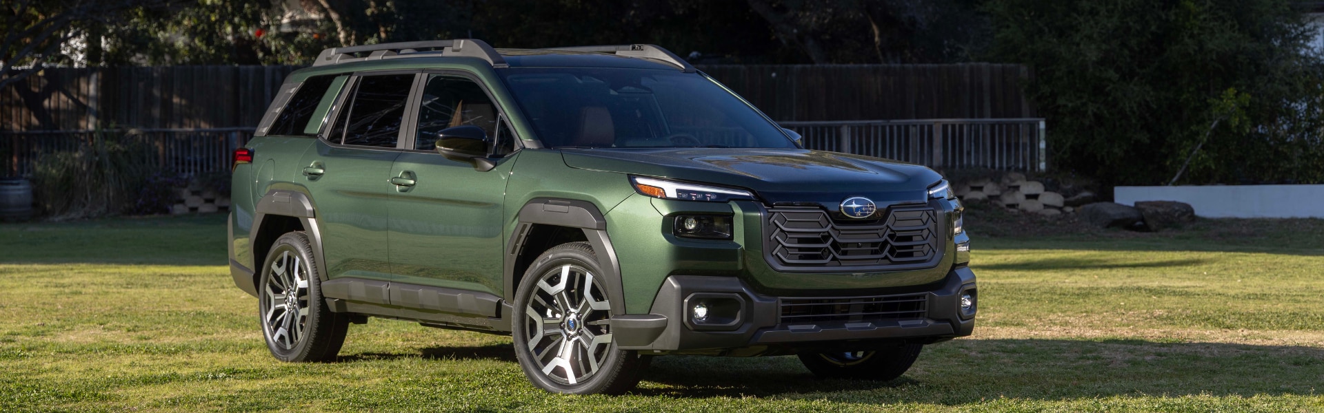 Green Subaru Outback parked on a field of grass