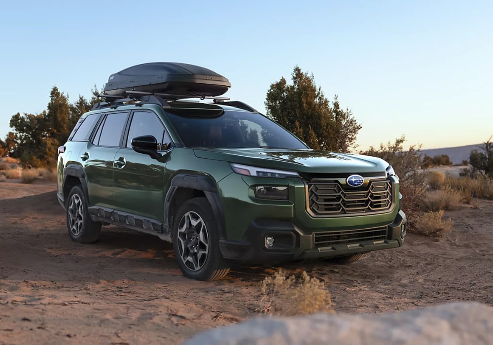 Green 2026 Subaru Outback parked on a dirt path. The car has a roof rack attached