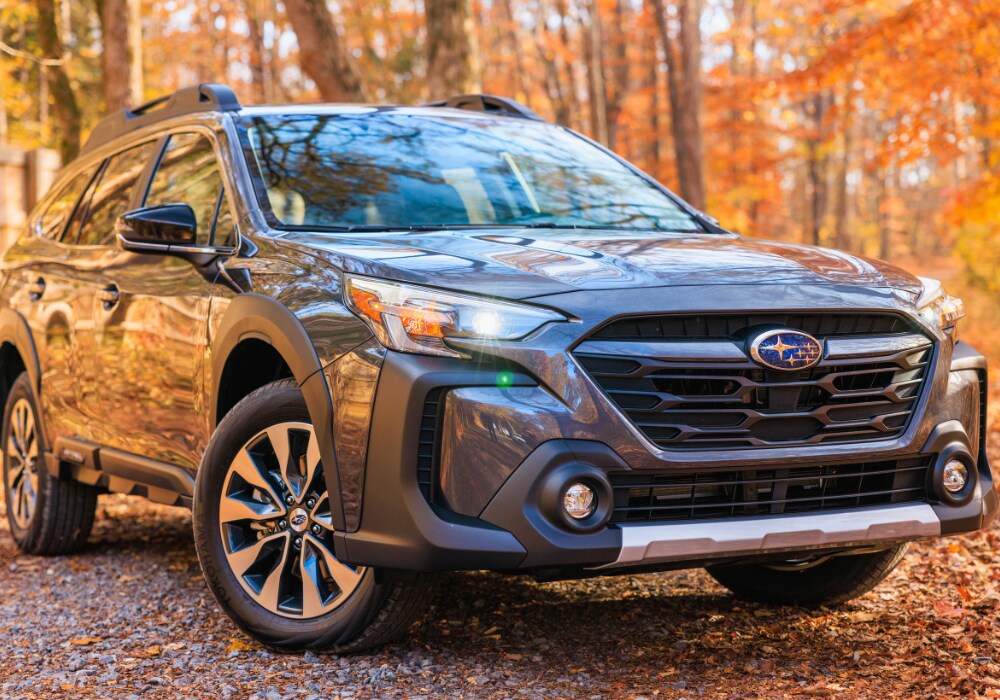 Close up shot of a Subaru Outback with its headlights on. The SUV is parked of a gravel road with leaves on the ground