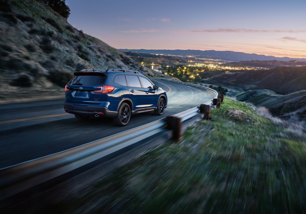 Rear view of a new Subaru Ascent driving down a road towards a city at night