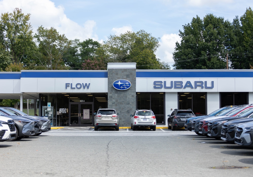 Storefront of Flow Subaru dealership in Winston-Salem, NC. The parking lot is full of Subaru cars for sale
