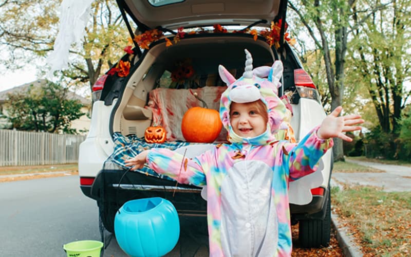 A child dressed in a unicorn Halloween costume posing in front of a decorated Subaru trunk