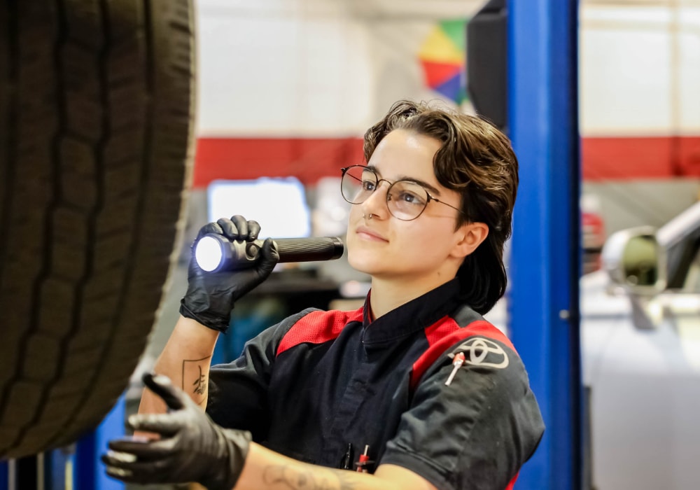A Toyota service technician shining a flashlight at the tire of a vehicle