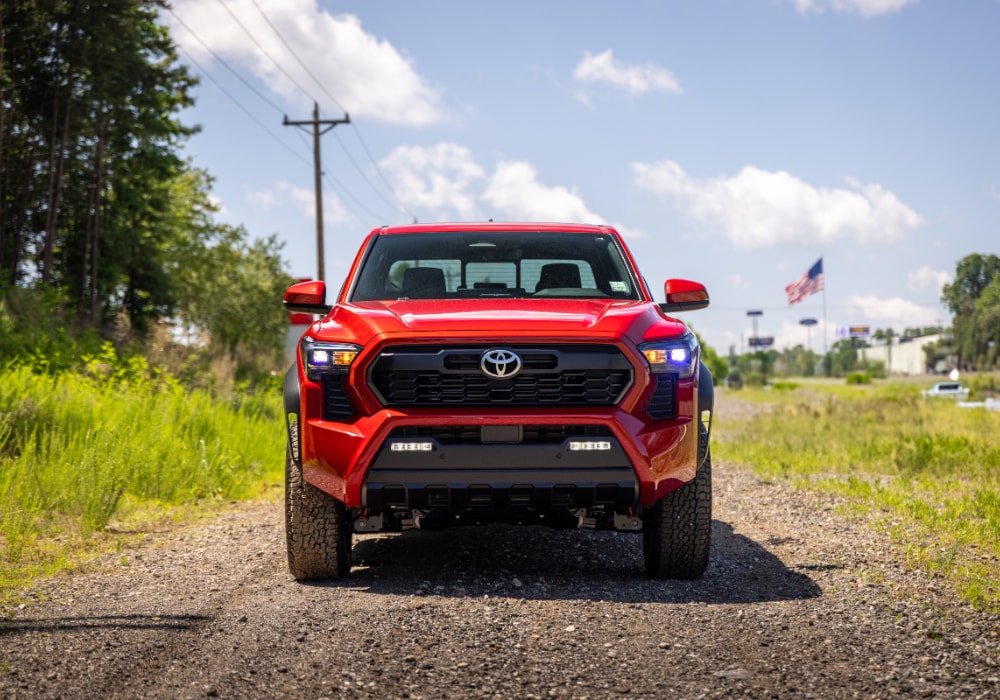 toyota-trucks-for-sale.png Red Toyota truck facing the camera parked on a gravek road