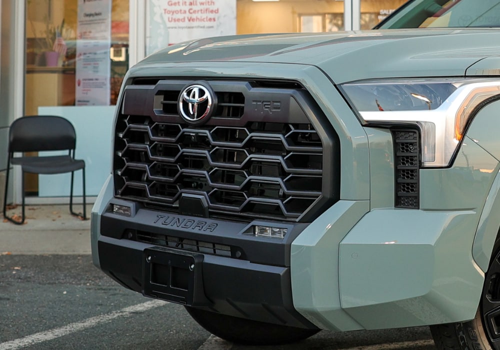 Close up photo of the front of a Toyota Tundra. The car is a light green color and the Toyota logo is visible on the front grille