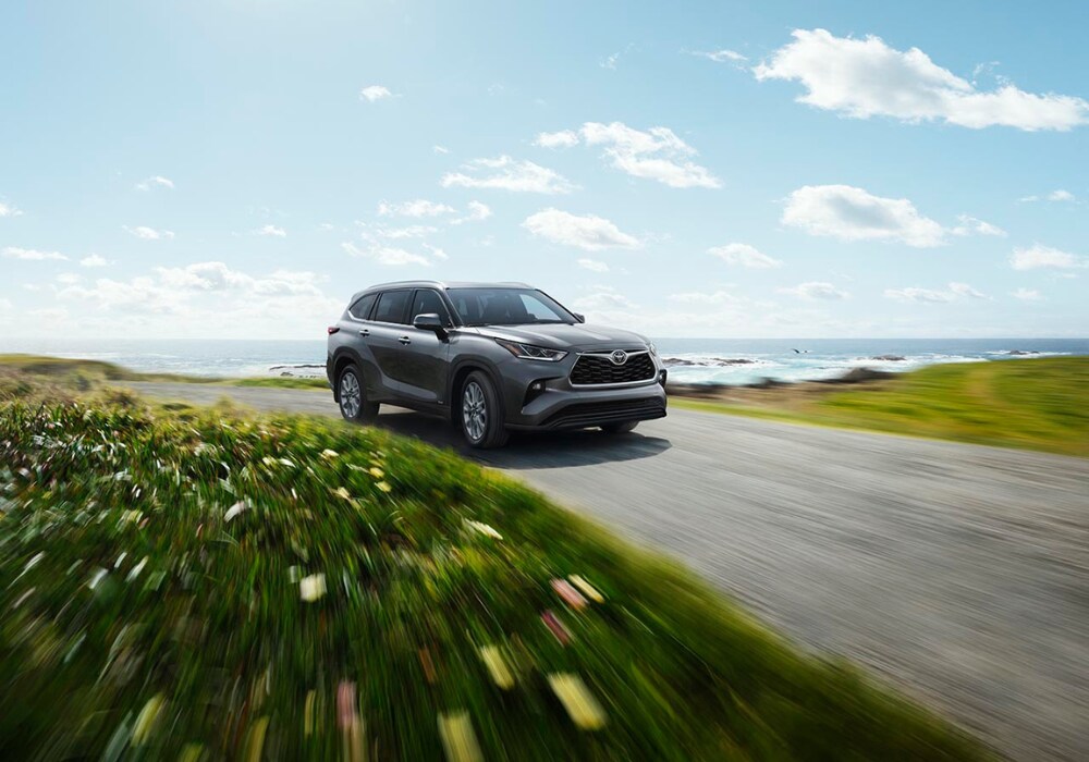 2025 Toyota Highlander driving down a road with a large body of water in the background