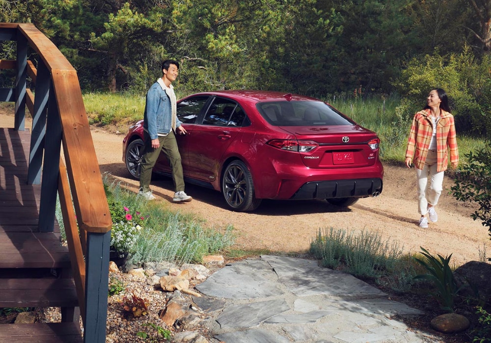 Red 2025 Toyota Corolla parked on a dirt road with a man and woman walking beside it