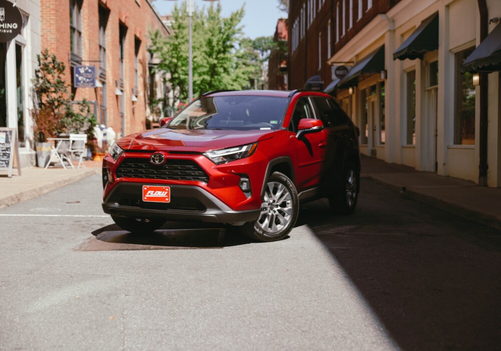 Red 2025 Toyota RAV4 parked on a city street. There is a Flow Automotive license plate on the front of the car
