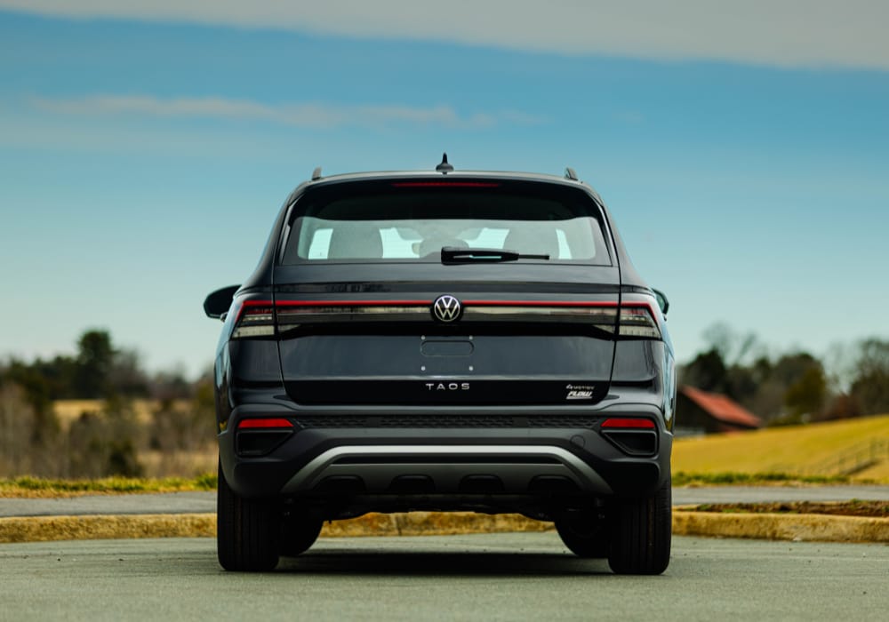 Back of the 2025 Volkswagen Taos. The SUV is black and there are trees in the background of the photo